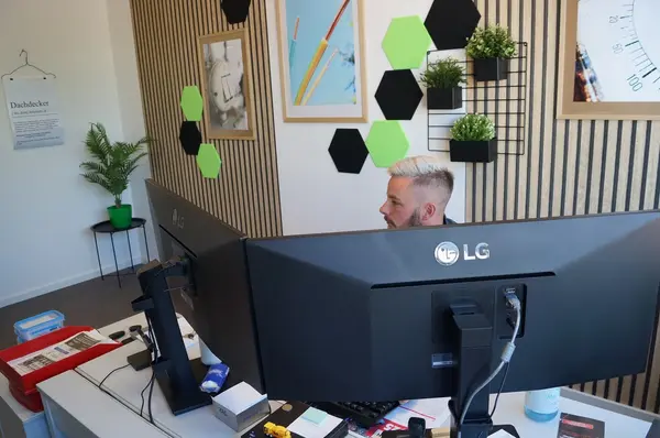 Mann arbeitet im modernen Büro mit zwei Monitoren, Pflanzen und kreativer Wanddekoration.