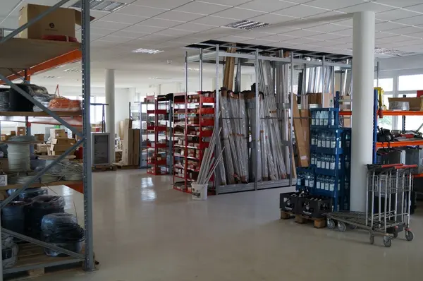 Modernes Lager mit Regalen, Kabeln, Baumaterialien und Wasserflaschen auf Paletten.