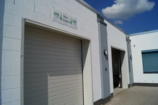 Moderne Warenannahme mit Rolltor an einem weißen Industriegebäude bei Sonnenschein.