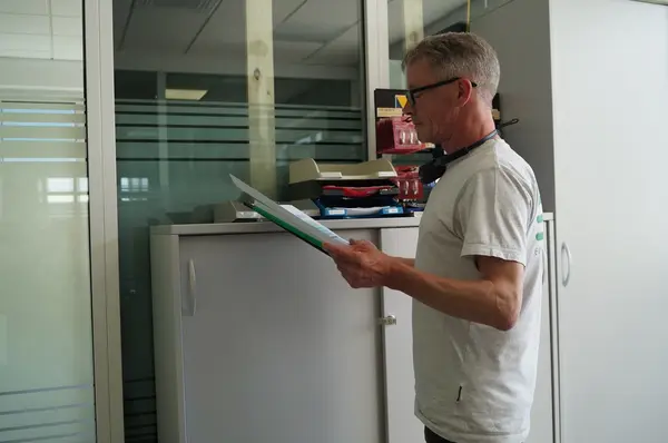 Ein Mann mit Kopfhörer liest in einem modernen Büro konzentriert ein Dokument am Aktenschrank.