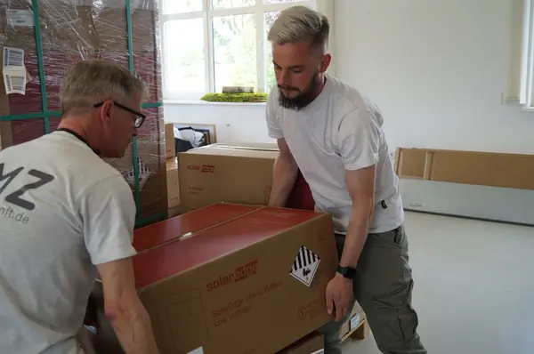 Zwei Männer heben im Lager gemeinsam eine SolarEdge Home Battery für Photovoltaikanlagen.