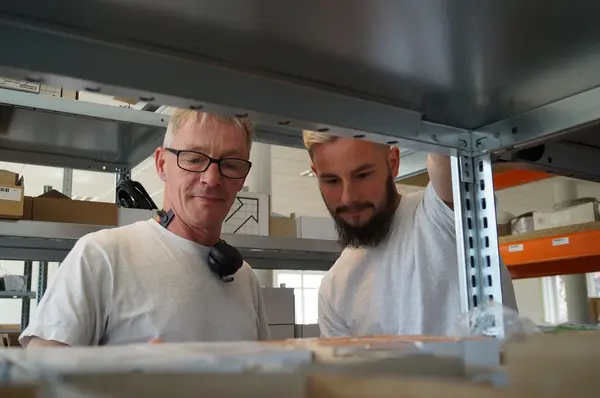 Zwei Männer arbeiten gemeinsam im Lager und sortieren Pakete im Industrie-Regal.