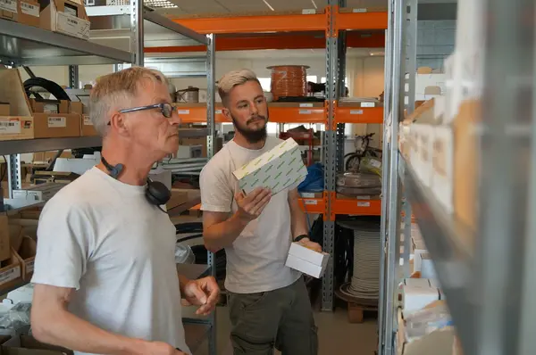 Zwei Männer prüfen Lagerbestände in einem modernen Lager mit Regalen und Verpackungen.