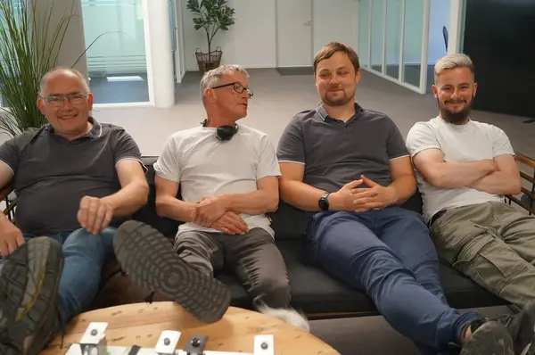 Vier Männer sitzen entspannt auf einem Sofa im modernen Büro und lächeln in die Kamera.